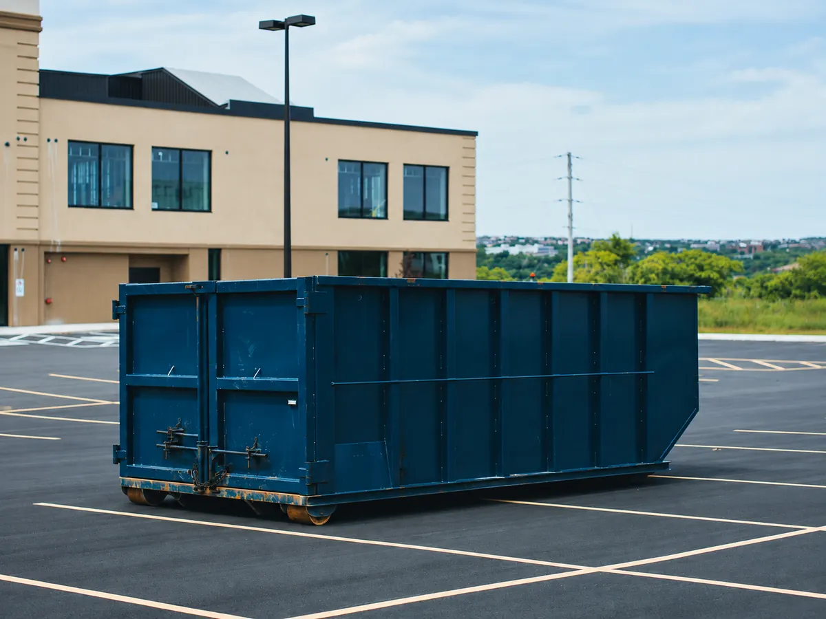 Blue roll-off dumpster in a paved lot beside a commercial building
